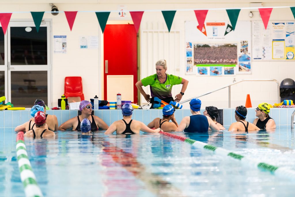 Women in pool receiving instruction from Coach